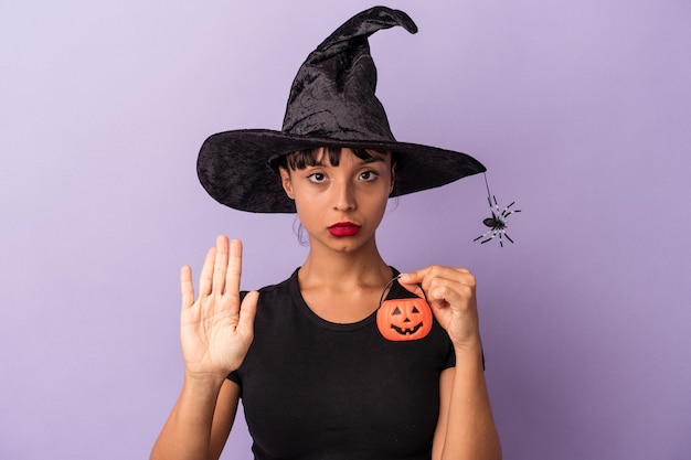 Young mixed race woman disguised as a witch isolated on purple background  standing with outstretched hand showing stop sign, preventing you.