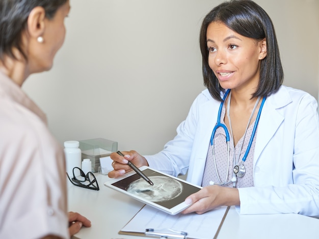 Young mixed race woman doctor gp in white medical uniform discussing results of mri with patient