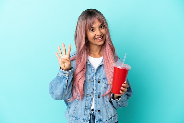 Young mixed race woman drinking a fresh drink isolated on blue background happy and counting four with fingers