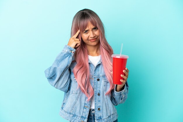 Young mixed race woman drinking a fresh drink isolated on blue background having doubts and thinking