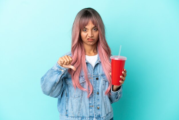 Young mixed race woman drinking a fresh drink isolated on blue background showing thumb down with negative expression