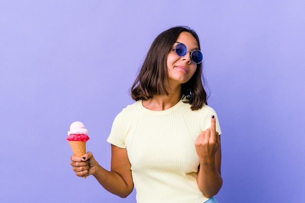 Young mixed race woman eating an ice cream pointing with finger at you as if inviting come closer.