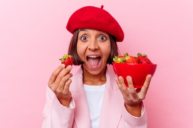 Young mixed race woman eating strawberry isolated on pink wall