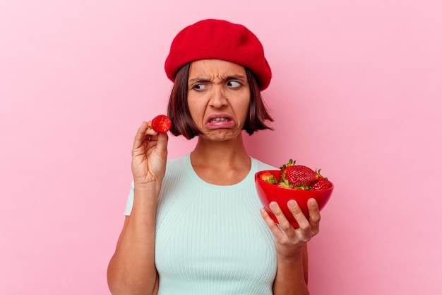 Young mixed race woman eating strawberry isolated on pink wall