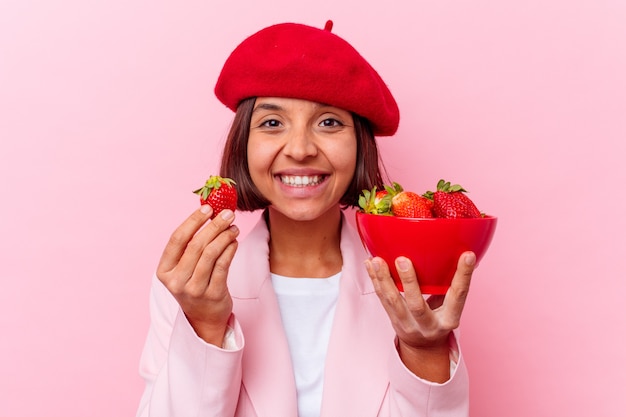 Young mixed race woman eating strawberry isolated on pink wall