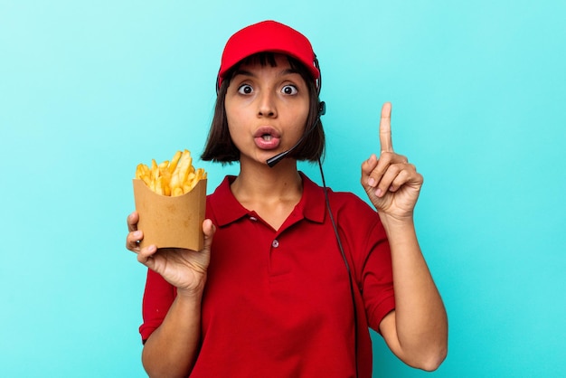 Young mixed race woman fast food restaurant worker holding\
fries isolated on blue background having some great idea, concept\
of creativity.