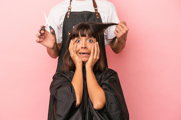 Foto giovane donna di razza mista che ottiene un taglio di capelli dal parrucchiere isolato su sfondo rosa