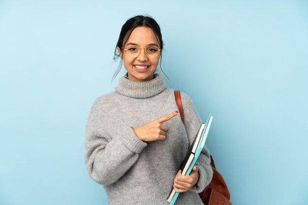 Young mixed race woman going to school on blue wall pointing to the side