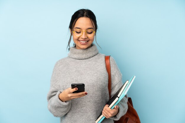 Young mixed race woman going to school on blue wall sending a message with the mobile