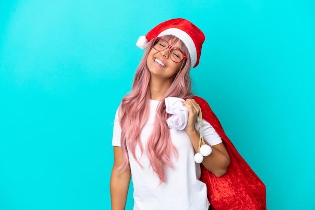 Young mixed race woman handing out gifts on Christmas isolated on blue background laughing