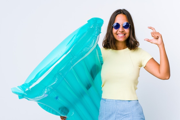 Young mixed race woman holding an air matress holding something little with forefingers, smiling and confident.