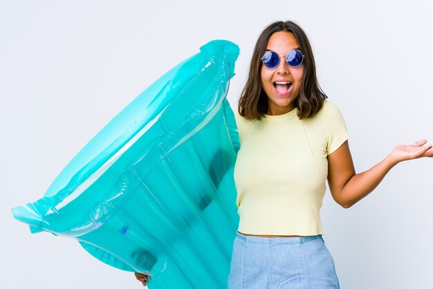 Young mixed race woman holding an air matress receiving a pleasant surprise, excited and raising hands.