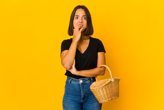 Young mixed race woman holding a basket biting fingernails, nervous and very anxious.