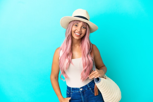 Young mixed race woman holding a beach bag with pamela isolated on blue background laughing