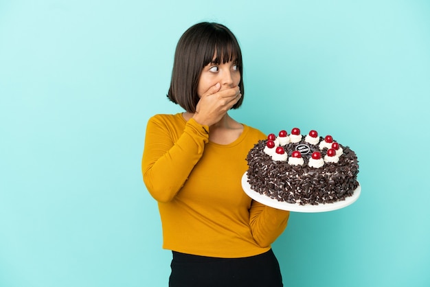 Young mixed race woman holding birthday cake covering mouth and looking to the side