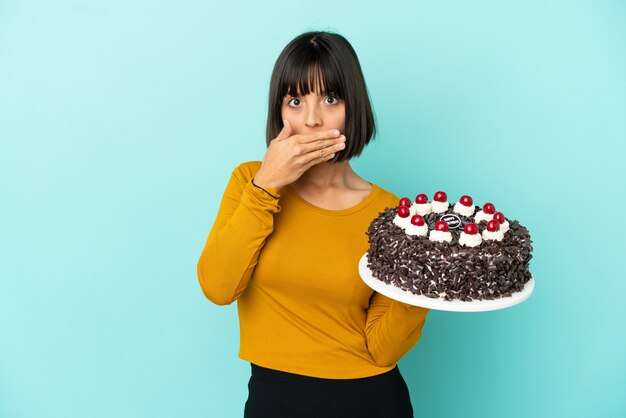 Young mixed race woman holding birthday cake covering mouth with hand