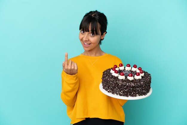 Giovane donna della corsa mista che tiene la torta di compleanno che fa il gesto venente