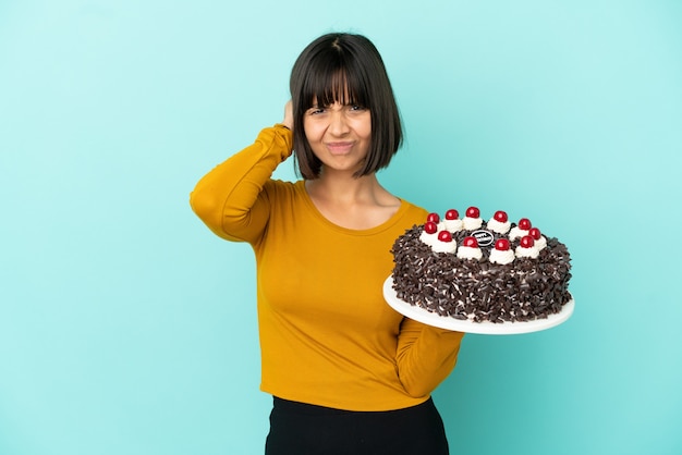 Giovane donna di razza mista che tiene la torta di compleanno frustrata e copre le orecchie