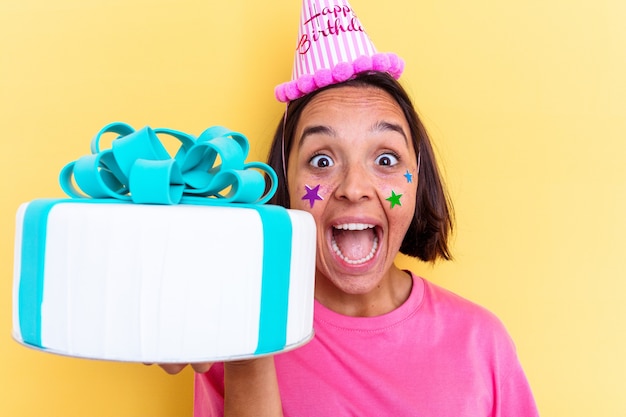 Foto giovane donna di razza mista che tiene una torta di compleanno isolata su priorità bassa gialla