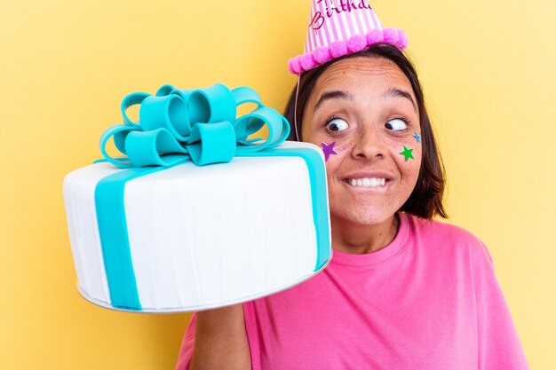 Giovane donna di razza mista che tiene una torta di compleanno isolata sulla parete gialla