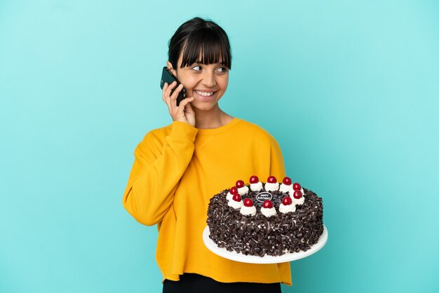 Young mixed race woman holding birthday cake keeping a conversation with the mobile phone with someone