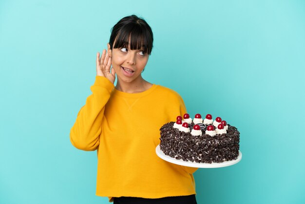 Young mixed race woman holding birthday cake listening to something by putting hand on the ear