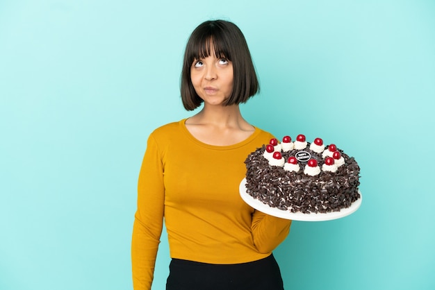 Giovane donna di razza mista che tiene in mano una torta di compleanno e guarda in alto