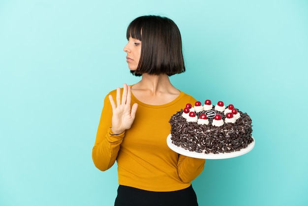Young mixed race woman holding birthday cake making stop gesture and disappointed