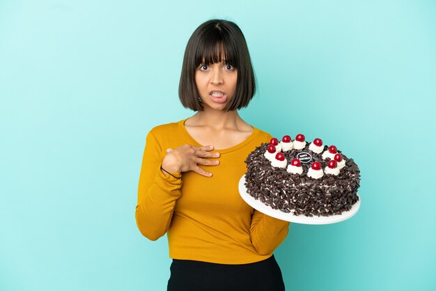 Young mixed race woman holding birthday cake pointing to oneself