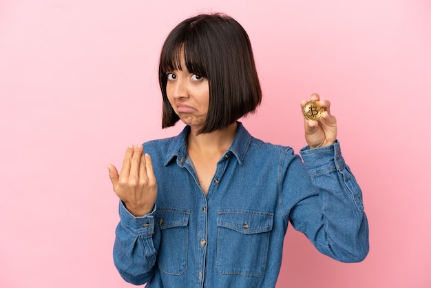 Photo young mixed race woman holding a bitcoin isolated background inviting to come with hand. happy that you came