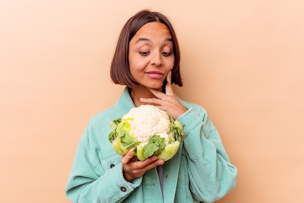 Young mixed race woman holding a cabbage isolated on beige background