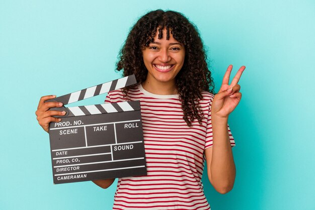 Young mixed race woman holding a clapperboard isolated on blue background showing number two with fingers.