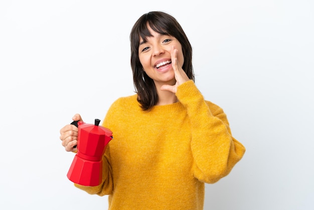 Young mixed race woman holding coffee pot isolated on white background shouting with mouth wide open