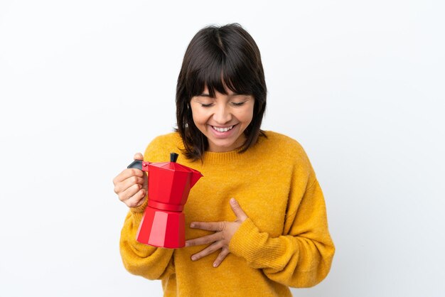 Young mixed race woman holding coffee pot isolated on white background smiling a lot