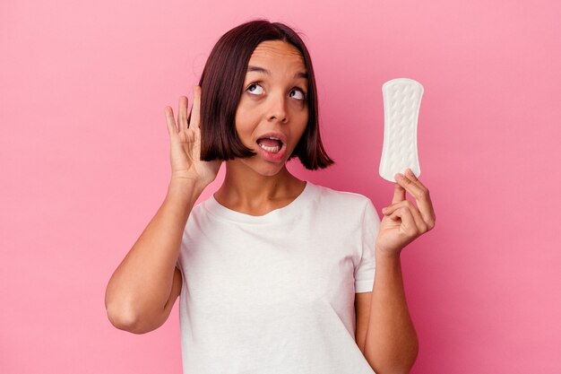 Young mixed race woman holding a compress isolated on pink wall trying to listening a gossip