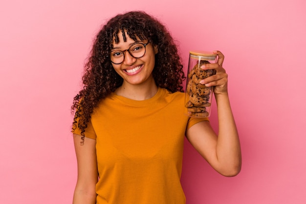 Young mixed race woman holding a cookies jar isolated on pink wall happy, smiling and cheerful.