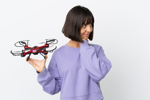 Young mixed race woman holding a drone isolated on white background looking up while smiling