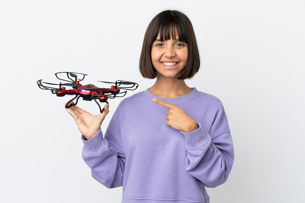 Young mixed race woman holding a drone isolated on white background pointing to the side to present a product