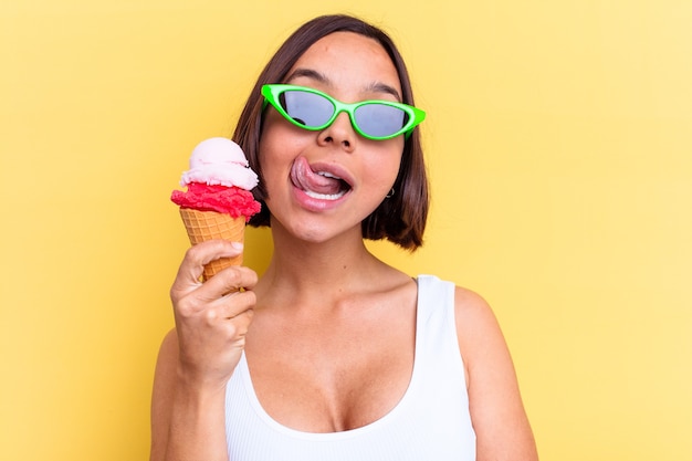 Young mixed race woman holding an ice cream isolated on yellow background