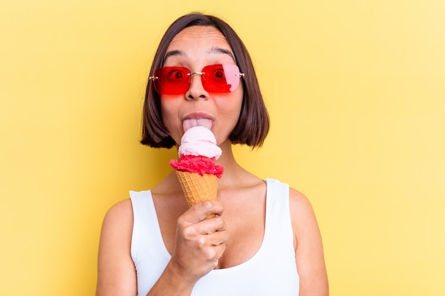 Young mixed race woman holding an ice cream isolated on yellow background