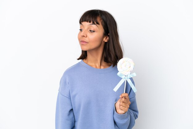 Young mixed race woman holding a lollipop isolated on white background looking to the side