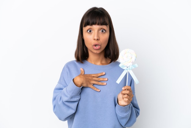 Young mixed race woman holding a lollipop isolated on white background surprised and shocked while looking right