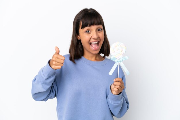 Young mixed race woman holding a lollipop isolated on white background with thumbs up because something good has happened