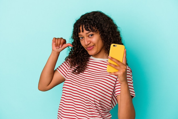 Young mixed race woman holding a mobile phone isolated on blue background feels proud and self confident, example to follow.