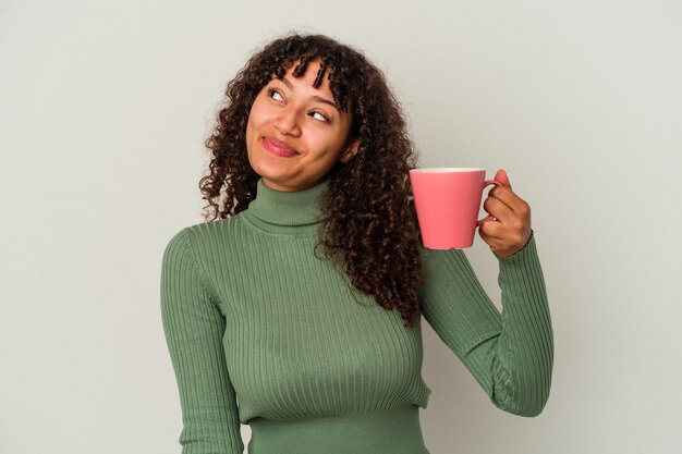 Young mixed race woman holding a mug isolated on white background dreaming of achieving goals and purposes