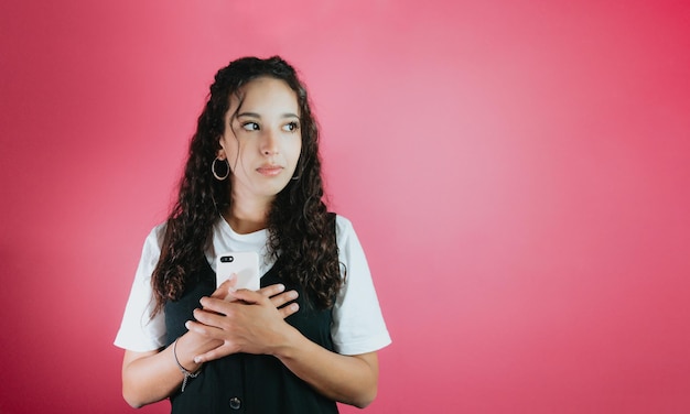 Young mixed race woman holding a phone worried about a message she just received, pink background removable background, minimal image, copy space, basic situations and feelings expressions