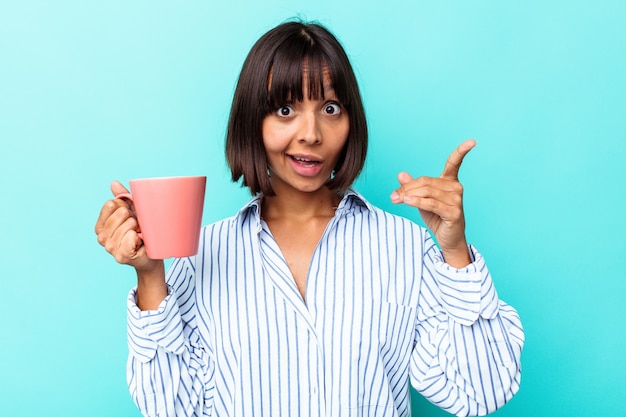 Young mixed race woman holding a pink mug isolated on blue background having an idea, inspiration concept.
