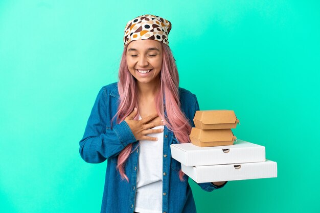 Photo young mixed race woman holding pizzas and burgers isolated on green background smiling a lot