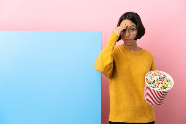 Молодая женщина смешанной расы, держащая попкорн с большим баннером на изолированном фоне, кое-что поняла и намеревается решить