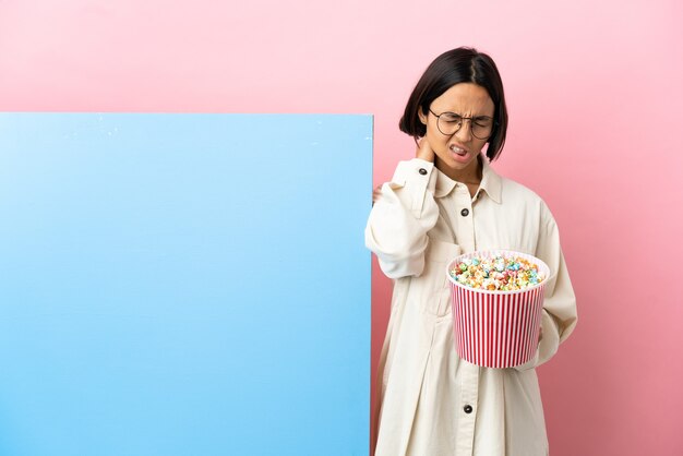 Young mixed race woman holding popcorns with a big banner isolated background with neckache